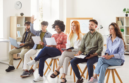 Business team participates in an office meeting, with members raising hands to ask and answer questions. The group collaborates, showcasing teamwork and professional work in a business environment.の写真素材