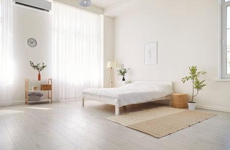Empty bedroom at home featuring a comfortable bed with white linens. The cozy and inviting interior is filled with morning light, creating a sense of peace and tranquility in the house space.の写真素材