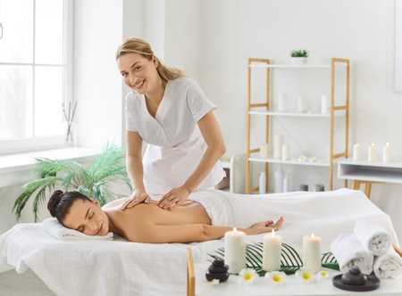 Woman masseur doing relaxing massage for client for body relaxing, posing in cosmetology spa centre. Relaxed female enjoing aroma therapy on couch. Health care and massaging conceptの写真素材