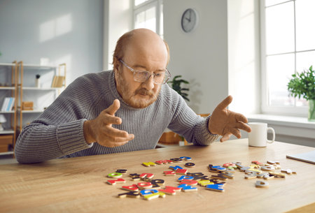 Senior man with dementia doing puzzles as a brain and memory training activity. Old bald bearded man in glasses sitting at a table and making up words with alphabet letters Alzheimers disease conceptの写真素材