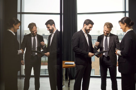 Man joyfully signing document while engaging in lively conversation with his colleagues in office. Male and female colleagues in professional business attire with smiles are having conversation.の写真素材