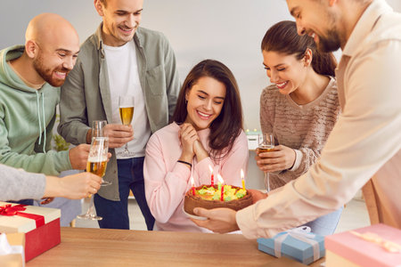 A group of young people give a woman a cake with candles, close-up. Friends congratulate you on your birthday. The woman appreciates congratulations. Gifts and birthday greetings conceptの写真素材