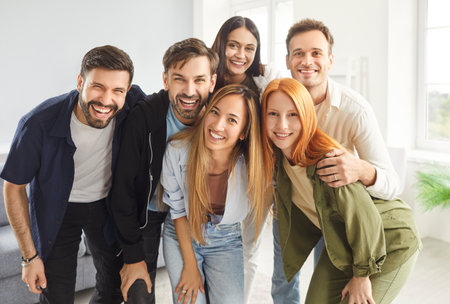 Group portrait of smiling friends, students or colleagues in casual clothes standing together, hugging each other and looking at camera. Happy young people making group photo during weekend hangout.の写真素材