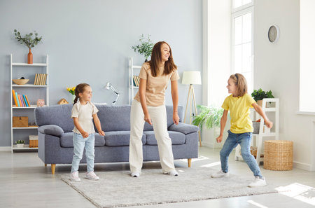 Young happy Caucasian mother having fun and dancing with her children in the living room at home. Woman parent enjoying spending time with kids. Family leisure and mothers day concept.の写真素材