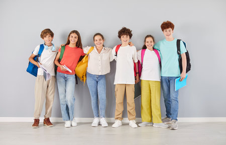 Group portrait of happy school children in colorful clothes standing together in row and hugging each other. Joyful smiling boys and girls with backpacks looking at camera and making group photo.の写真素材