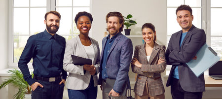 Happy diverse business team standing in the office. Five cheerful confident successful people in smart casual suits smiling and posing for a group photo all together. Banner. Work and success conceptの写真素材