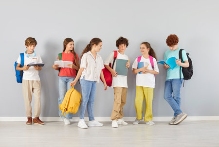 School children, young student friends and classmates girls and boys standing together at wall with rucksacks enjoy friendly educational environment, loving team communication, wearing casual wearの写真素材