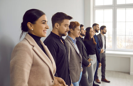 Side view of happy, young, beautiful business lady standing next to her smiling colleagues. Row of...