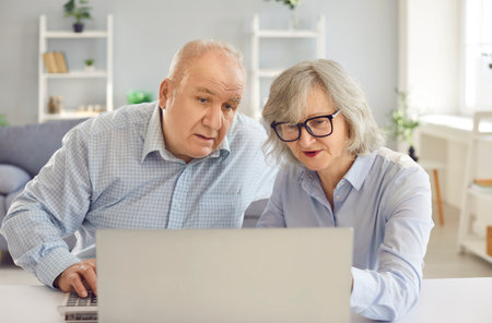 Elderly senior couple sitting at the table with laptop calculating finances planning family budget...