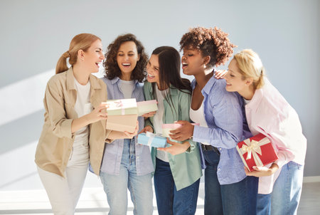 Group of cheerful multiracial women exchanging wrapped gift boxes, laughing and celebrating special ocasion together. Happy female friends holding presents on birthday or International Women Day.の写真素材