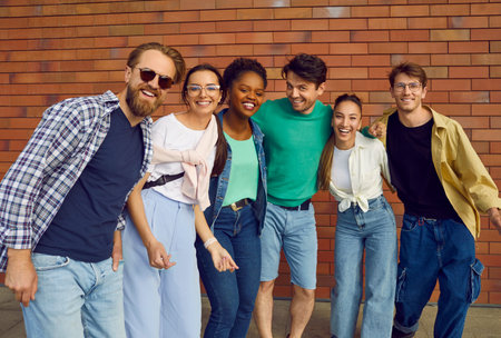 Hanging out with friends. Portrait of carefree multiracial friends in casual clothes on background of brick wall. Cheerful men and women having fun standing in row hugging and smiling at camera.の写真素材