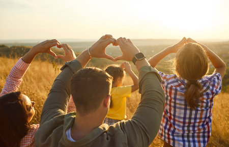 Happy family outdoors at sunset share love togetherness. Parents and children raise arms to form heart shapes in nature, smiling in warm summer light. Celebrating family unity, love, happiness.の写真素材