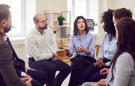 Group of office workers is holding a meeting, sitting in circle in office. People team engaged in...
