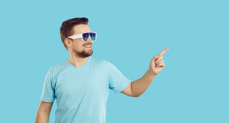 Smiling young Caucasian man in sunglasses isolated on blue studio background point at good sale deal...