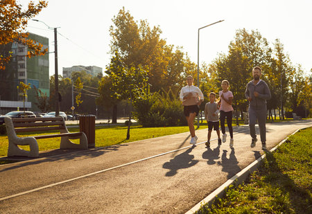 Family running with children jogging outdoors together. In a sunny park, they enjoy fitness...