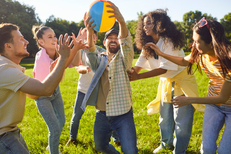 Happy joyful young people friends in casual clothes having fun in the summer park. Smiling men and women catching ball playing together outdoors on holidays. People and leisure in nature concept.の写真素材