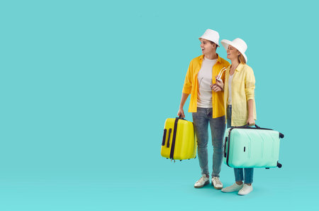 Couple of cheerful tourists. Joyful couple with luggage enjoying their exciting summer trip isolated on light blue background. Full length woman and man with suitcases stare in amazement at copy spaceの写真素材