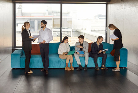 Confident young business people men and women talking preparing for meeting and discussing work project. Company employees group communicating with each other sitting on sofa in modern office.の写真素材