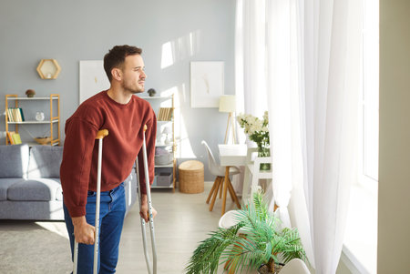 Broken leg or foot injury trauma man walking on crutches window looking at home, patient on rehabilitation period, painful swollen foot, not be able to walk on it, severe fracture, protective coverの写真素材