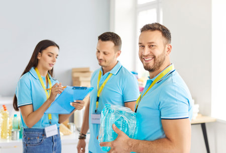 Happy male volunteer with mineral water six pack working together with other volunteers for food charity non profit organization that supplies homeless shelters and refugee centers. Donation conceptの写真素材