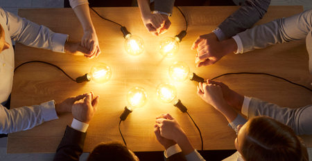 Cropped top view on group of business professionals sitting around wooden desk, holding hands in...