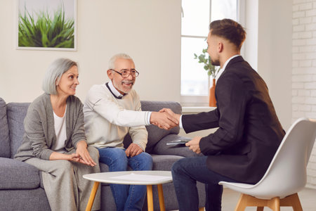 Elderly couple warmly doing handshake with real estate agent sealing deal on their new home purchase. Handshake symbolizes trust and satisfaction marking beginning of their exciting journey handshakeの写真素材
