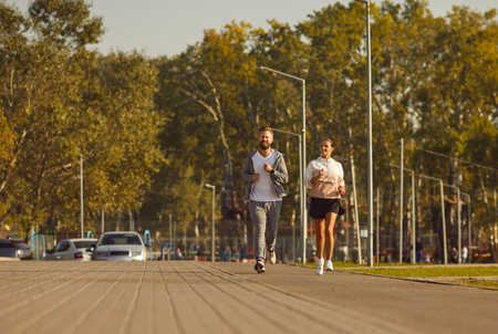 Couple running in park during morning workout. They run at pace on a promenade, enjoying fitness and...