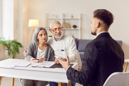 Senior couple listening to young professional consultant helping advising on right legal solutions. Elderly people at desk with paper, document, male lawyer, adviser or solicitor providing informationの写真素材