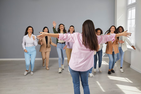 Diverse female business team celebrating success of their colleague. Group of cheerful excited exhilarated girls run to hug and congratulate happy young woman on her achievement and career promotionの写真素材