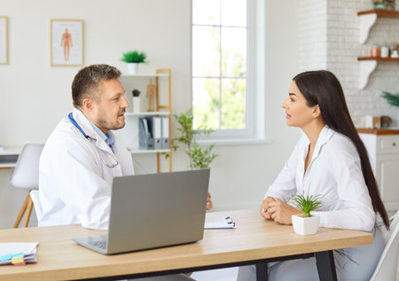 Doctor or nurse provides medical consultation to a female patient in a hospital office. Visit focuses on healthcare support and patient care, with professional advice during the medical visit.の写真素材