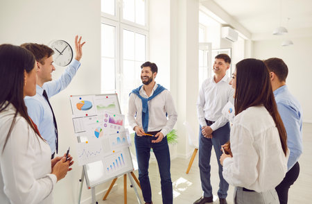 Successful business people on flip charts presentation of new project in boardroom at company meeting. Happy coach auditor speaks with diverse colleagues about business using board, graphs, planningの写真素材