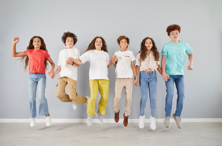 Portrait of a group of happy schoolchildren is playing and holding hands while spending time together in a leisure activity on grey background. Friendship, unity, and joyful interaction.の写真素材