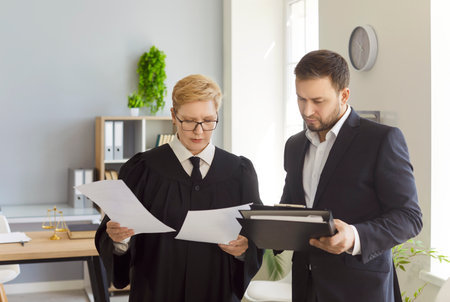 Female judge looking through legal documents standing with man lawyer in office. Mature woman court...