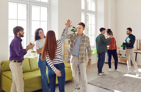 Two groups of happy looking friends standing and chatting in big spacious room. Diverse group of...