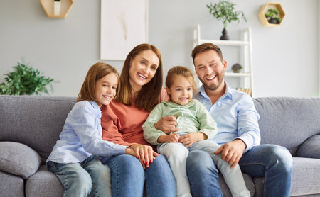 Portrait of happy smiling married couple sitting on sofa in the living room at home with their two...