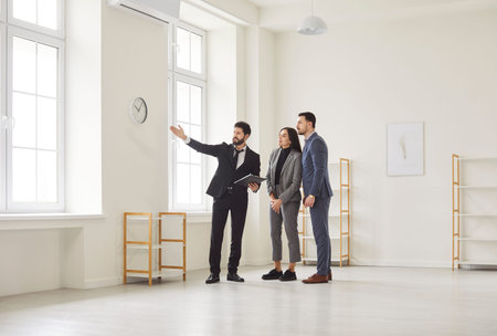 Realtor showing house to a young happy couple looking at the view from the window. Professional real...