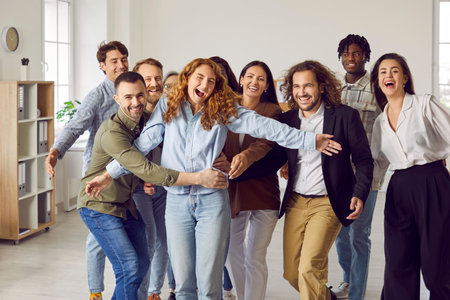 Happy business team having fun together. Group of cheerful, joyful, excited diverse colleagues and friends hugging in the office all together. Concept of friendship and teamworkの写真素材