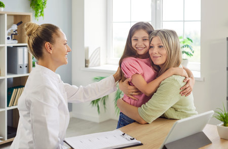 Pediatrician observes mother hug child after consultation. Smiling family doctor shares reassuring results in medical clinic. Positive pediatric care, support and reassurance.の写真素材