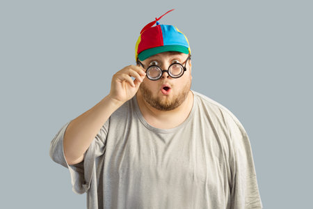 Surprised shocked funny man with glasses and hat. Mouth agape, he wears propeller beanie with...