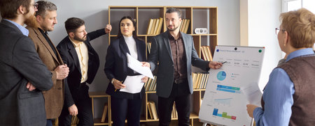 Team trainer hosts meeting presentation with colleagues. A coach and speaker review charts on flip...