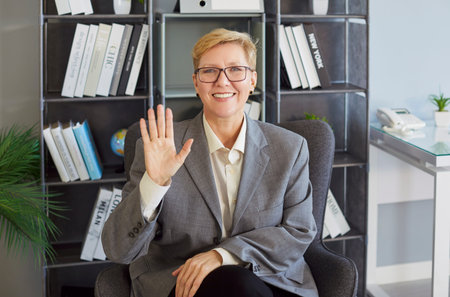 Business woman greeting on video call waving hand during webinar. Smiling worker gives a wave in...