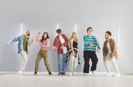 Energetic women and men friends dancing against grey wall in dance studio, learning new modern...