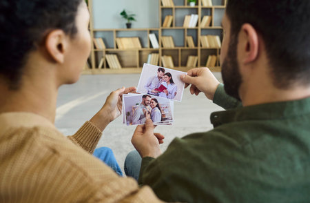 Couple holding photos and family prints at home. They review snapshots together, recalling memories...