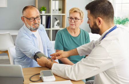 A doctor measuring patients blood pressure and discusses results with a smiling senior couple in a...