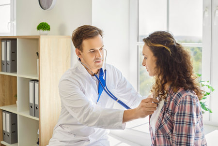 Doctor listens to patient with stethoscope on exam. In medical clinic, the physician checks chest...