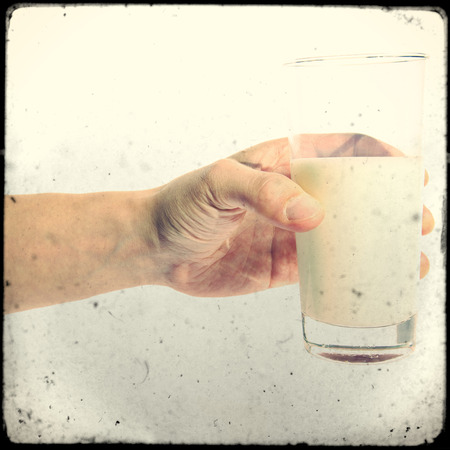 Glass of milk in hand against white backgroundの写真素材