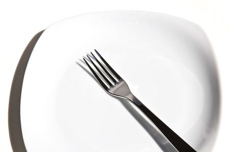  A white plate with silver fork. Close up