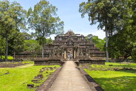A stone walkway leads to the ancient Phimeanakas Temple in Angkor Thom, surrounded by trees and greeneryの写真素材