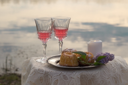 Two pink glas of wine, candle and lilac on the table outdoorsの写真素材