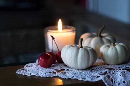 autumn and winter cozy table decoration with candle, small apples and white baby boo pumpkinsの写真素材